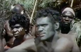 The white actor is seen with a blackened face sitting in front of Aboriginal actors.