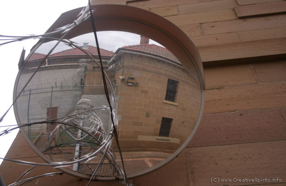 A mirror reflecting barbed wire and prison buildings.