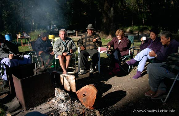 A group of Aboriginal people sit around a camp fire.