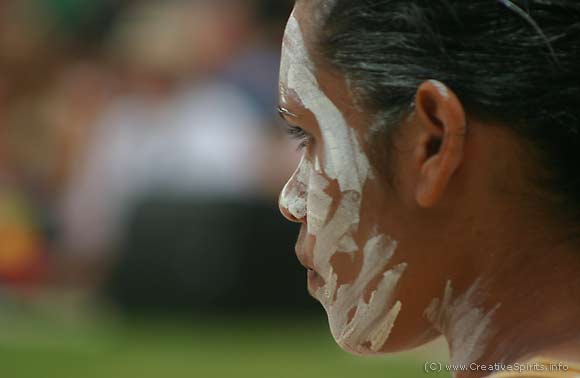 An Aboriginal woman with ochre marks in her face looking into the distance.