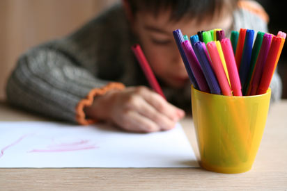 Child drawing a picture, pens in foreground.