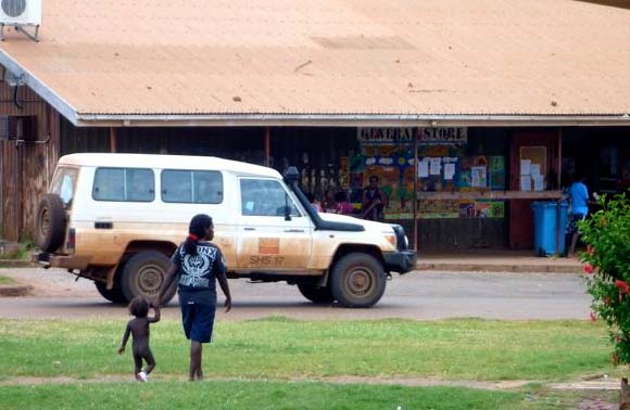 Two people walk in front of the General Store where a 4WD is parked.