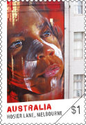 Next to a column of windows in a multi-storey building is a giant image of an Aboriginal boy's face painted with ochre.