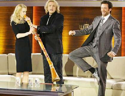 Actress Nicole Kidman blows the didgeridoo while actor Hugh Jackman imitates an Aboriginal man standing on one leg.