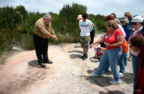 Les Bursill pointing to a rock engraving with tour participants looking on.