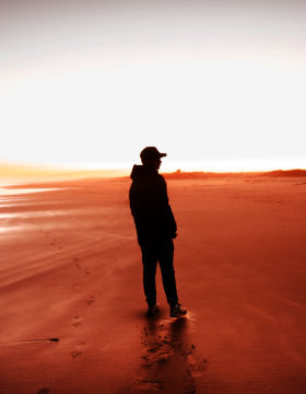 The black silhouette of a man walking on a red sandy beach.