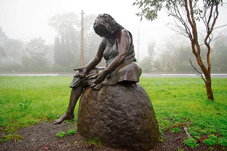 Figure of a grieving mother sitting on a rock with her hands empty.
