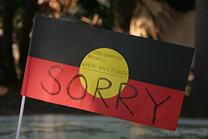 An Aboriginal flag with the words '1788: Genocide begins...when will it end? Sorry.'.