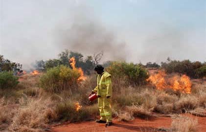An Aboriginal man lighting fires in dry bushland.