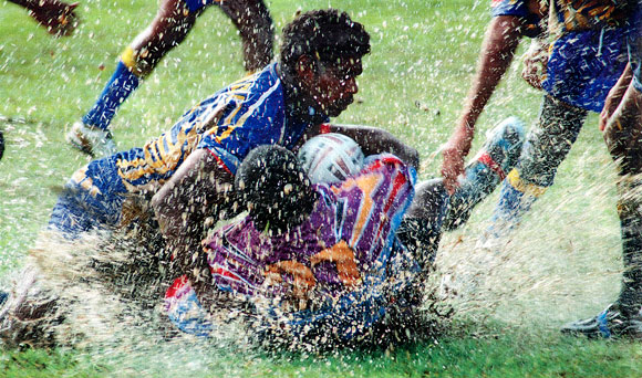 Indigenous players splash into puddles of water.